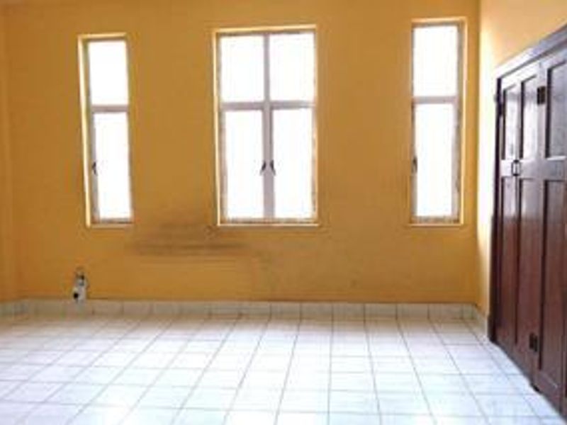 A vacant bedroom featuring tiled flooring, built-in wooden cabinetry, and three windows providing natural light.
