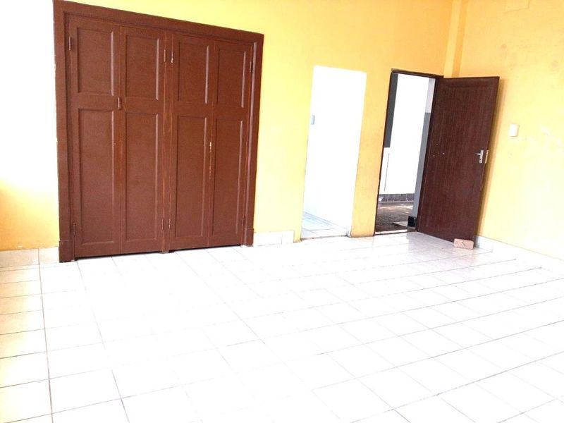 An empty room featuring tiled flooring, built-in wooden cabinetry, and access to adjacent spaces through internal doorways.