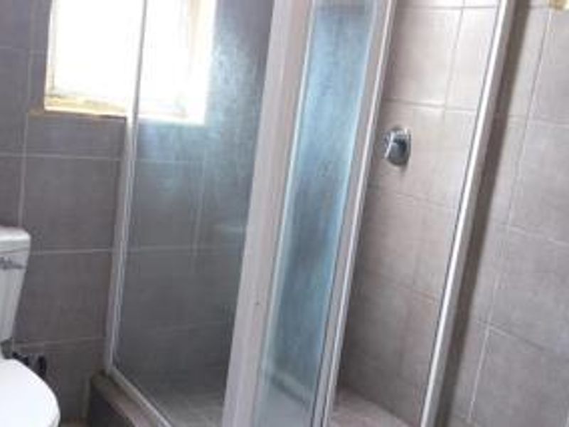 A functional bathroom featuring a tiled shower enclosure with a glass door and a standard toilet.