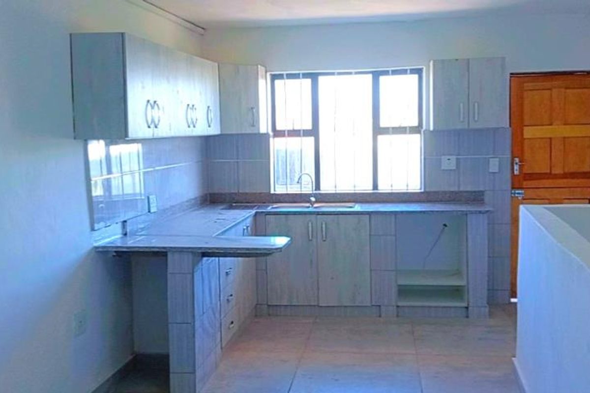 A functional kitchen area featuring built-in cabinetry, tiled countertops, a stainless steel sink, and a window providing natural light.