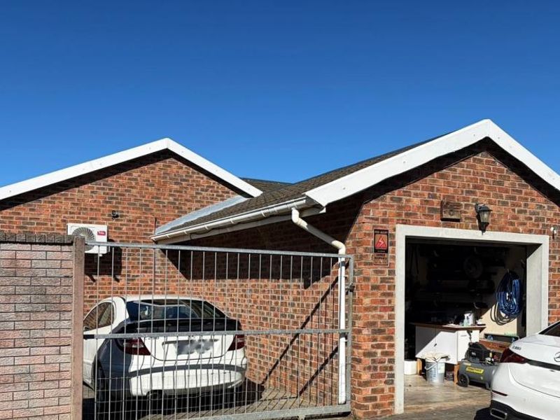Front exterior view of a face brick townhouse featuring a gabled roof, a secure gated parking area, and an integrated garage.