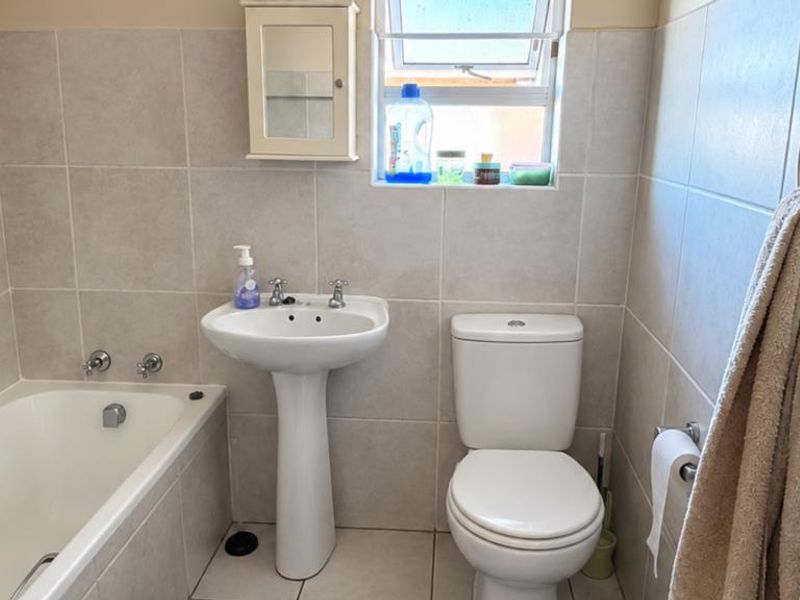 A functional bathroom featuring a pedestal basin, bathtub, and toilet with neutral wall and floor tiling.