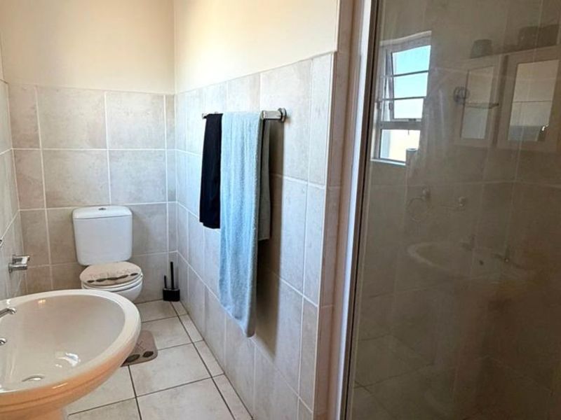 A functional bathroom featuring a pedestal basin, toilet, and a glass-enclosed shower with neutral wall and floor tiling.