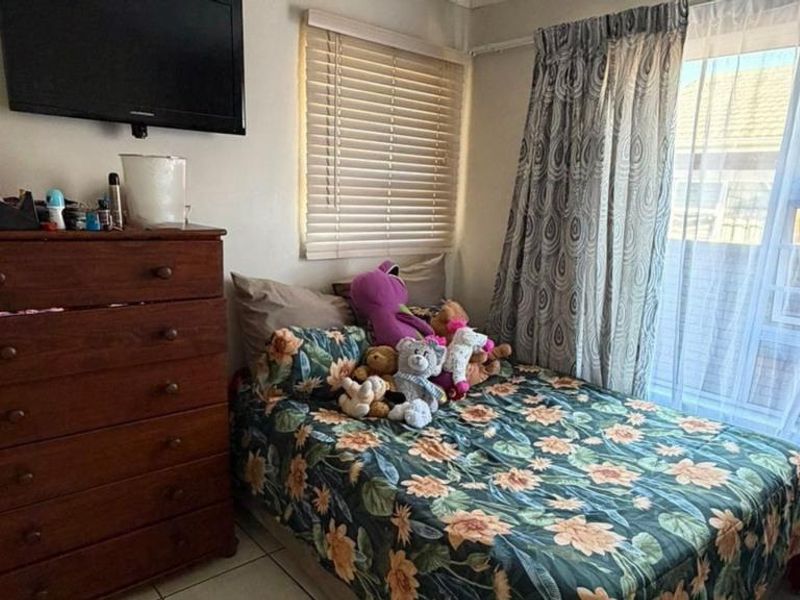 A compact bedroom featuring tiled flooring, a sliding window with venetian blinds, and neutral wall finishes.