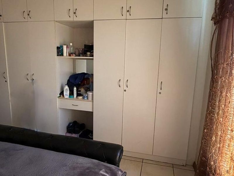 A bedroom featuring extensive white built-in cupboards with a central vanity nook and tiled flooring.