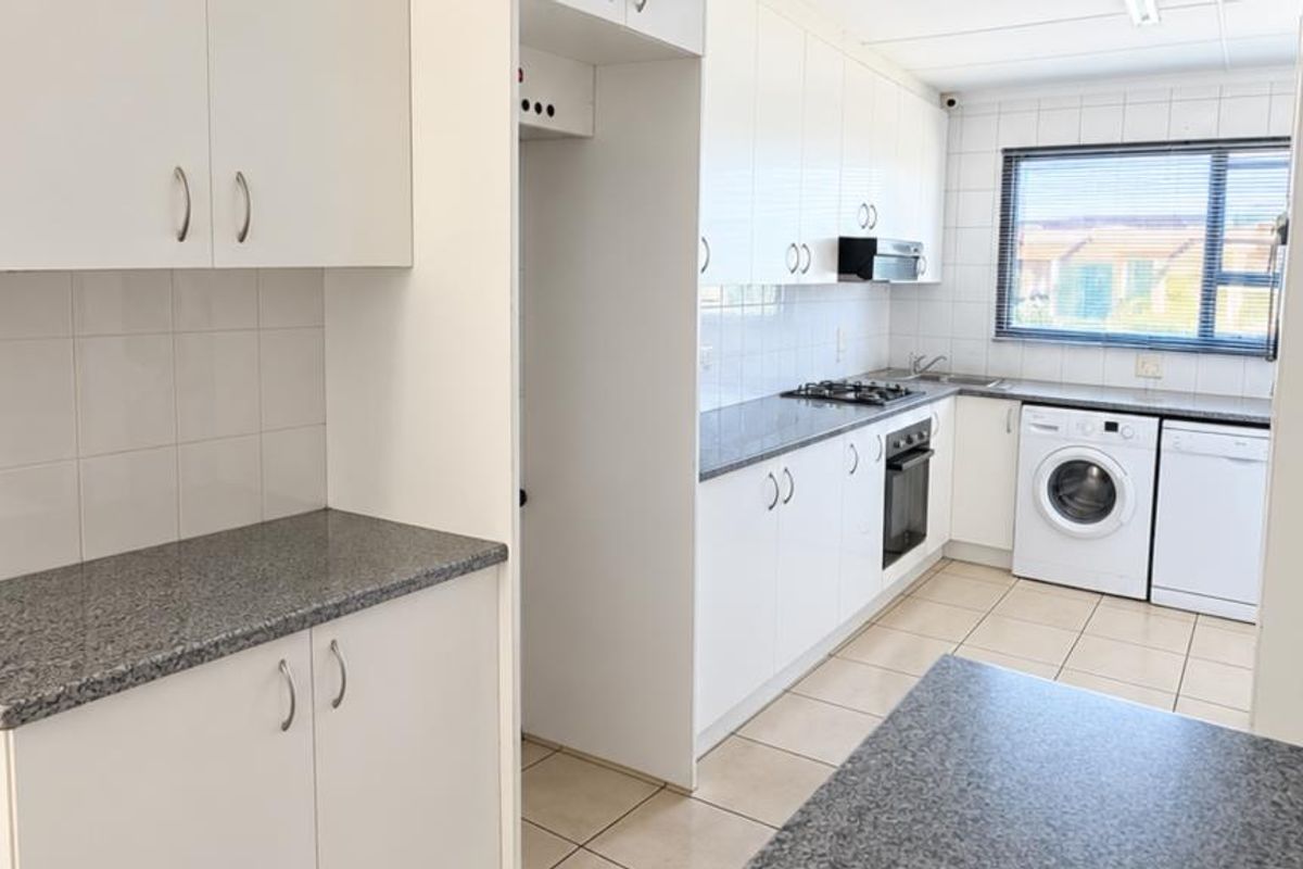 Functional kitchen featuring white cabinetry, granite countertops, gas hob, built-in oven, and tiled flooring with space for laundry appliances.