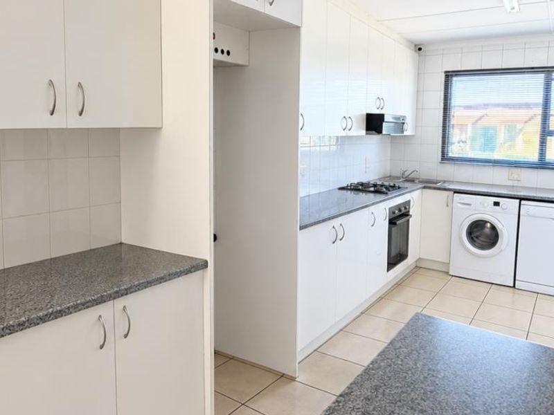 Functional kitchen featuring white cabinetry, granite countertops, gas hob, built-in oven, and tiled flooring with space for laundry appliances.
