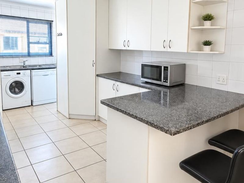 Functional kitchen featuring granite countertops, ample built-in cabinetry, a breakfast bar, and integrated laundry plumbing, finished with clean tiled flooring and backsplash.