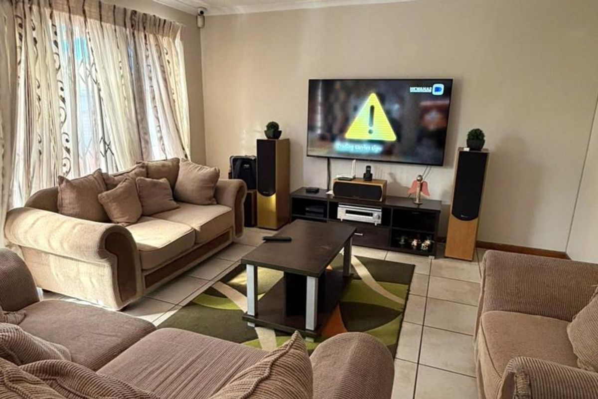 A comfortable living room featuring tiled flooring, large windows with curtain rails, and a security gate, providing a functional and well-lit space.
