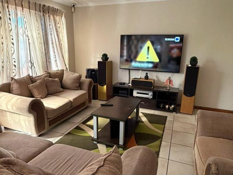 A comfortable living room featuring tiled flooring, large windows with curtain rails, and a security gate, providing a functional and well-lit space.