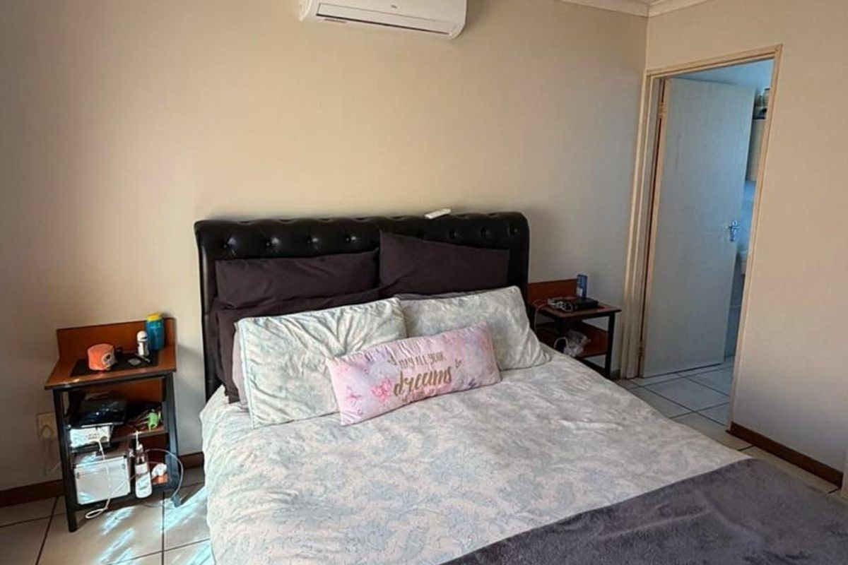 A functional bedroom featuring tiled flooring and a wall-mounted split-system air conditioner, with direct access to an adjoining room.