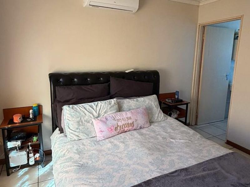 A functional bedroom featuring tiled flooring and a wall-mounted split-system air conditioner, with direct access to an adjoining room.