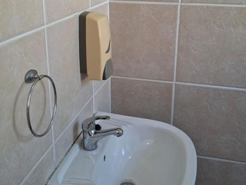 A functional bathroom space featuring a wall-mounted basin with a chrome mixer tap, towel ring, and neutral ceramic wall tiling.