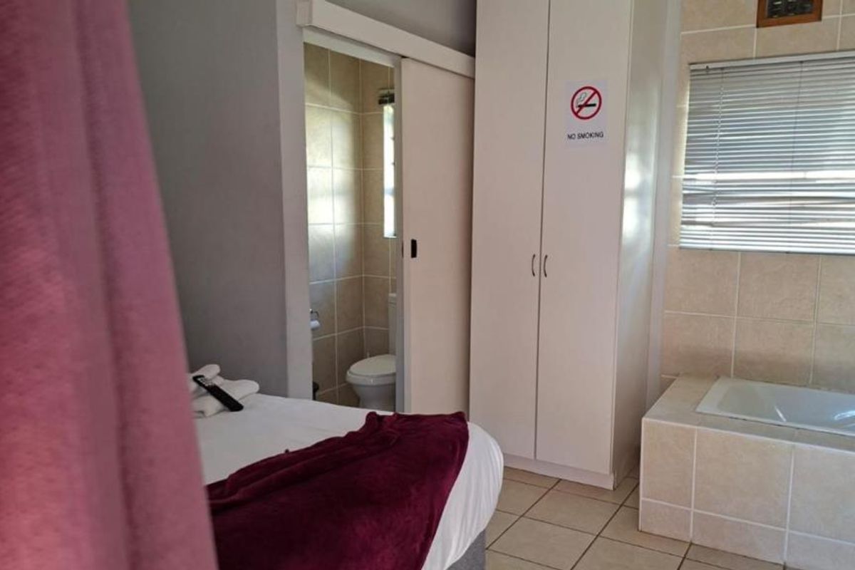 Bedroom featuring tiled flooring, a built-in wardrobe, and an integrated en-suite bathroom with a built-in bathtub and venetian blinds.