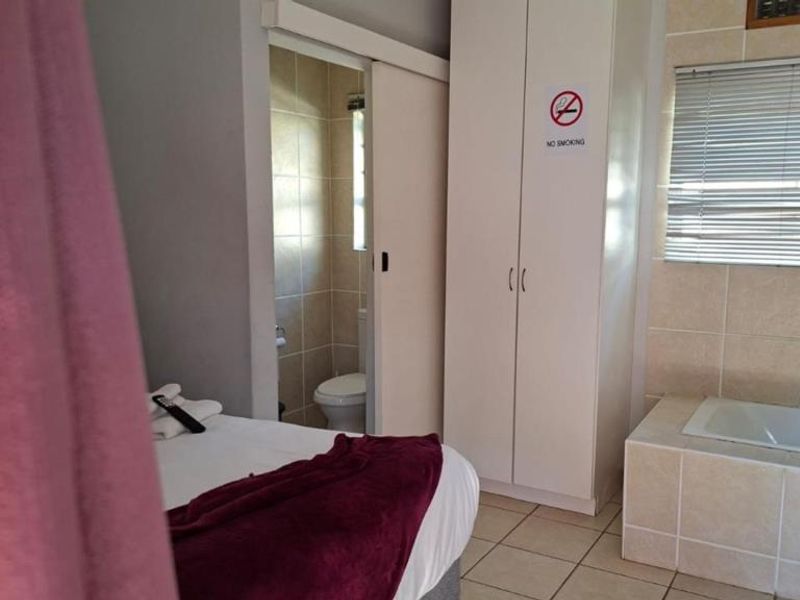 Bedroom featuring tiled flooring, a built-in wardrobe, and an integrated en-suite bathroom with a built-in bathtub and venetian blinds.