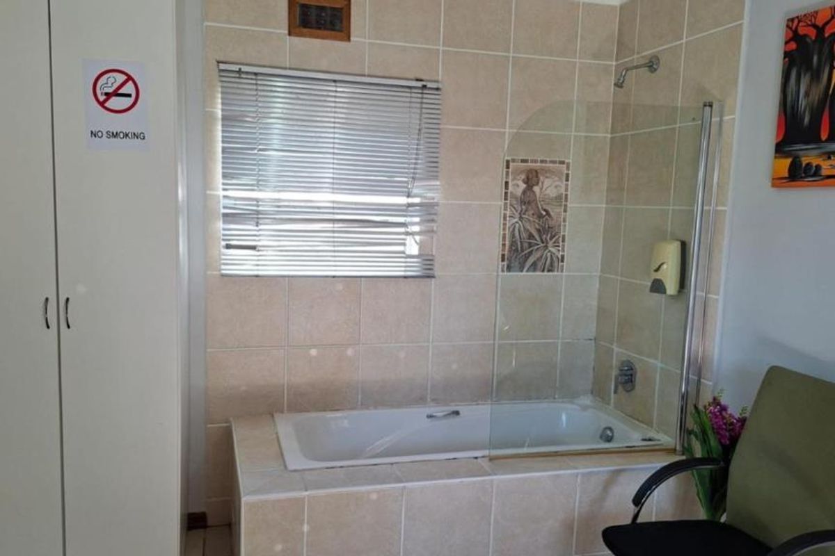 A functional bathroom featuring a built-in bathtub with a glass shower screen, tiled walls, and integrated storage cabinetry.