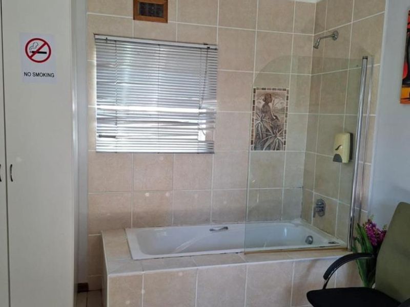 A functional bathroom featuring a built-in bathtub with a glass shower screen, tiled walls, and integrated storage cabinetry.
