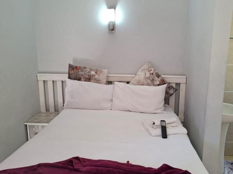 A bedroom featuring a built-in headboard and wall-mounted lighting, with an adjacent open-plan bathroom area containing a pedestal sink.