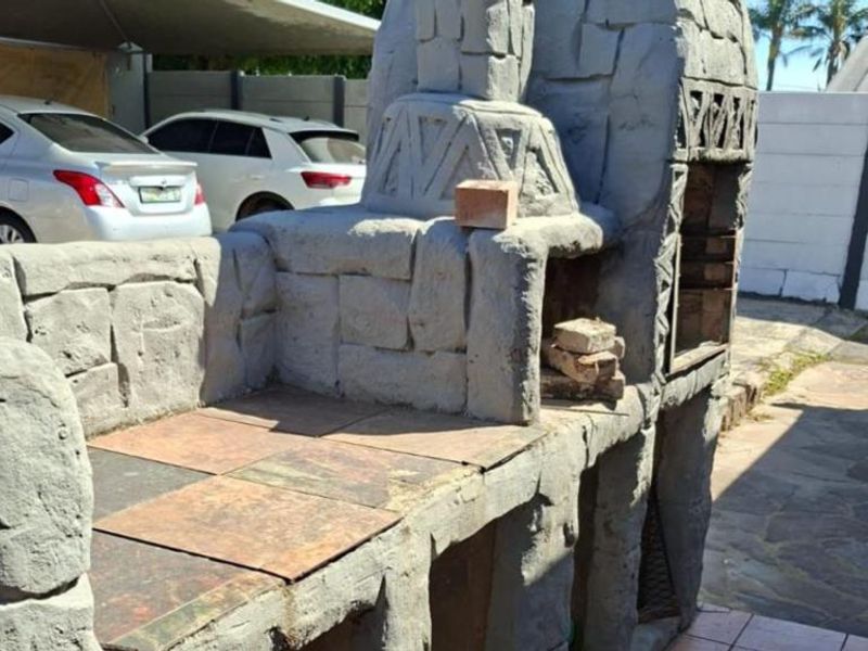 Outdoor area featuring a large, custom-built stone braai with integrated tiled prep space and paved flooring.