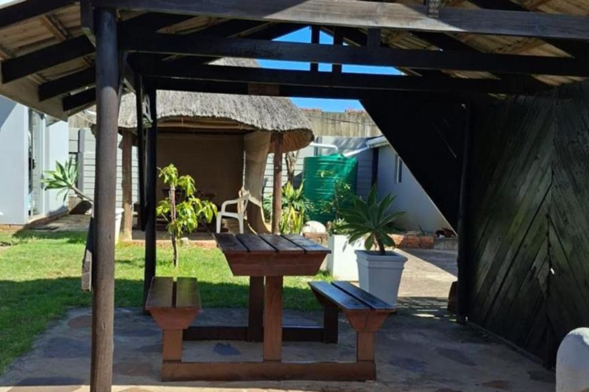 A rear garden area featuring a timber pergola, a traditional thatched lapa, paved patio space, and a water storage tank.