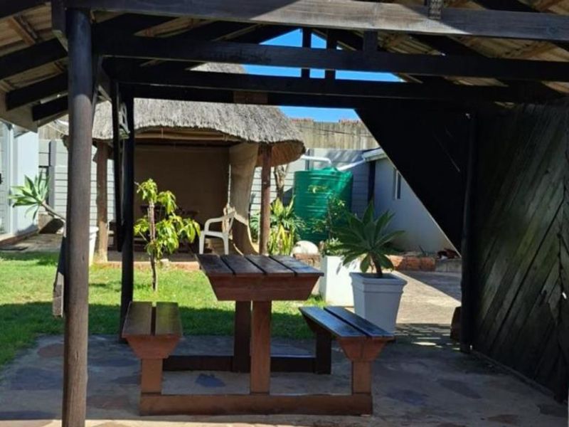 A rear garden area featuring a timber pergola, a traditional thatched lapa, paved patio space, and a water storage tank.