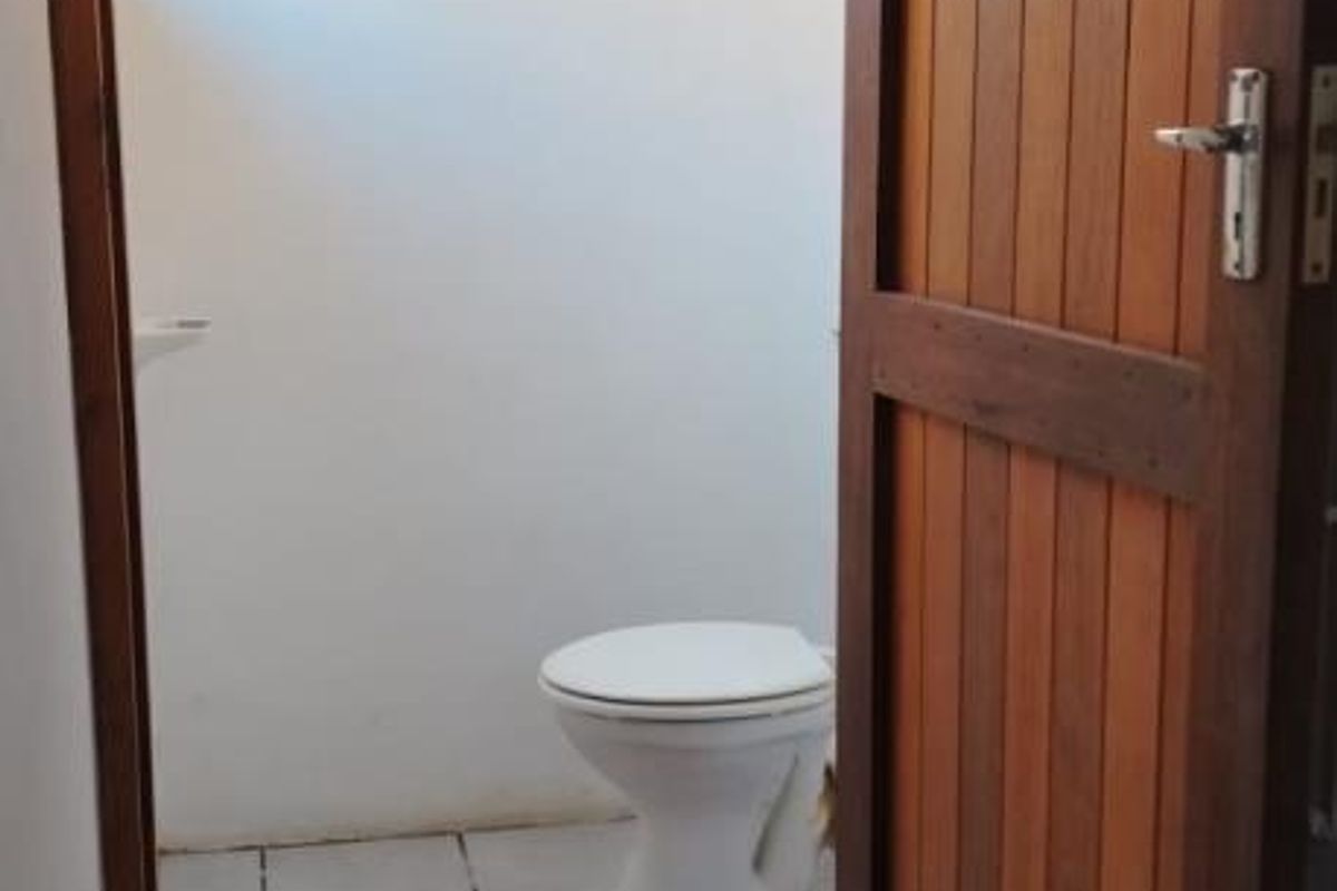 A functional bathroom featuring tiled flooring and a standard toilet, accessed through a solid timber door.