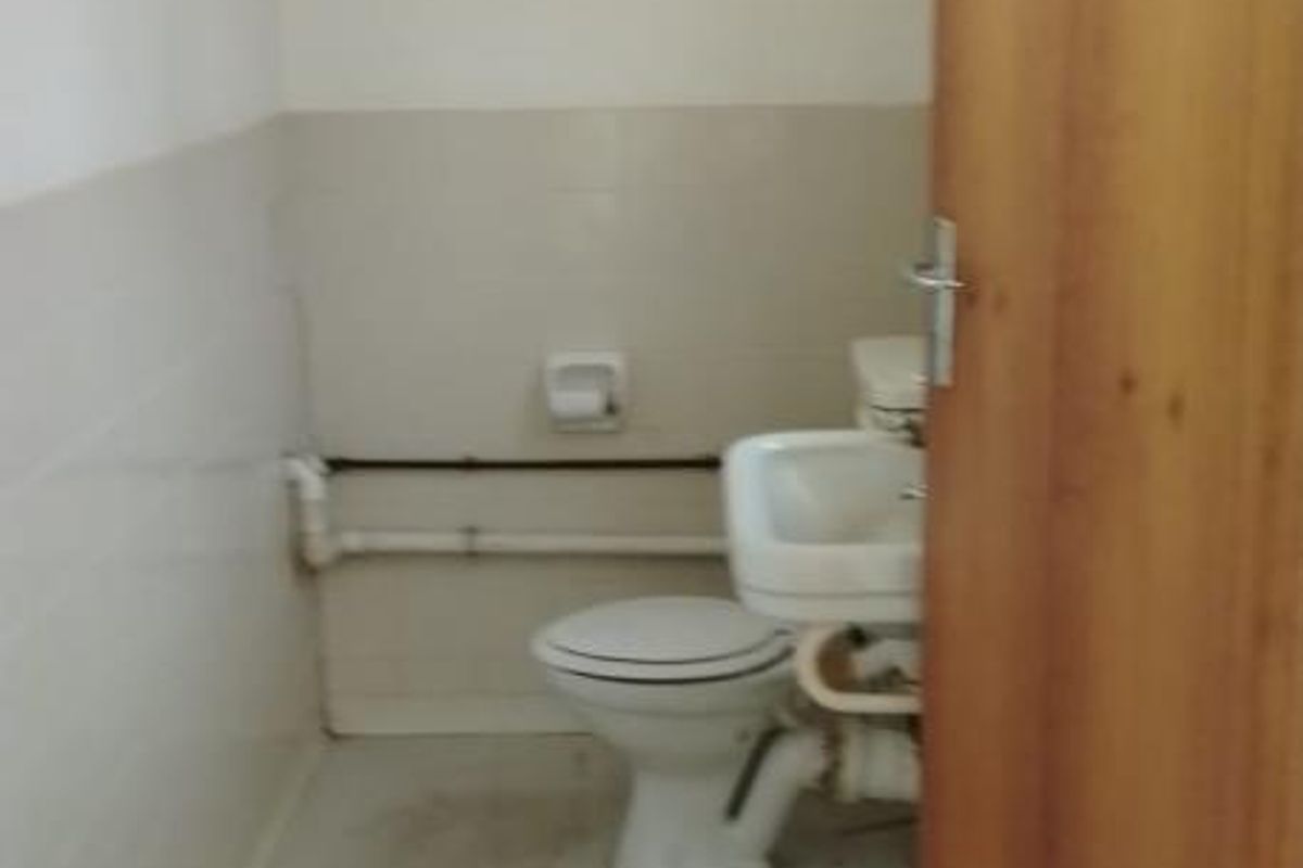 A small, functional commercial restroom featuring a standard toilet and wall-mounted basin with exposed plumbing fixtures.