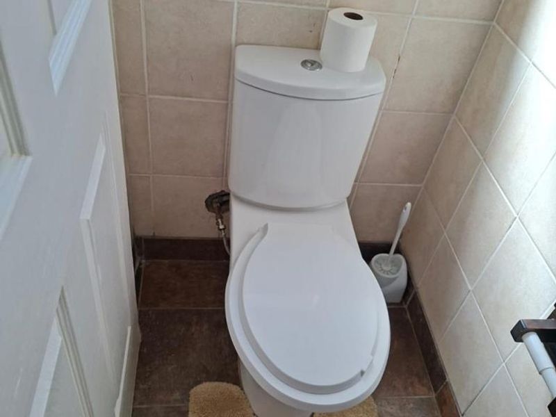 A compact bathroom featuring a standard white toilet, tiled walls, and tiled flooring.
