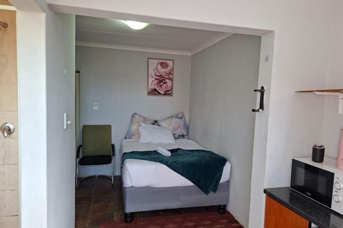 A compact bedroom area featuring tiled flooring, adjacent to a kitchen space, providing a functional living layout.