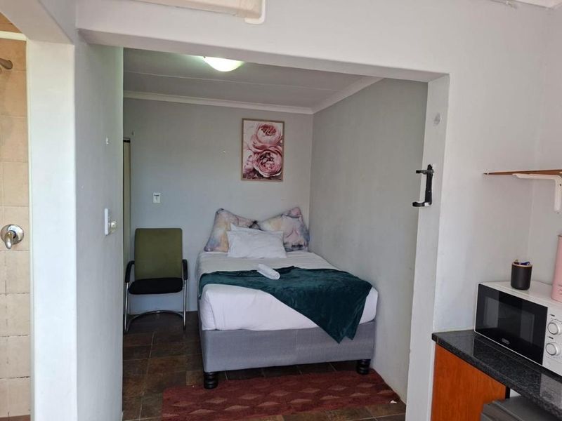 A compact bedroom area featuring tiled flooring, adjacent to a kitchen space, providing a functional living layout.