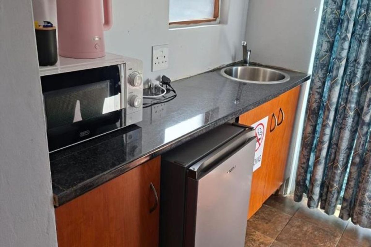Compact kitchenette featuring dark granite countertops, wooden cabinetry, a stainless steel sink, and tiled flooring.