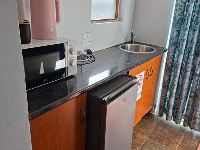 Compact kitchenette featuring dark granite countertops, wooden cabinetry, a stainless steel sink, and tiled flooring.