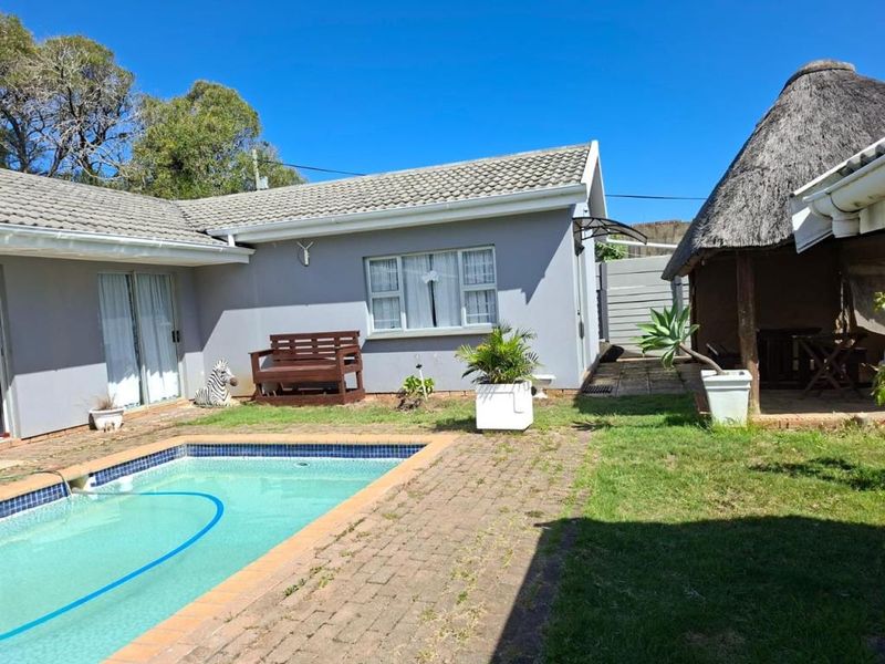 Outdoor area featuring a swimming pool, paved patio space, and a thatched lapa structure set against the rear building elevation.