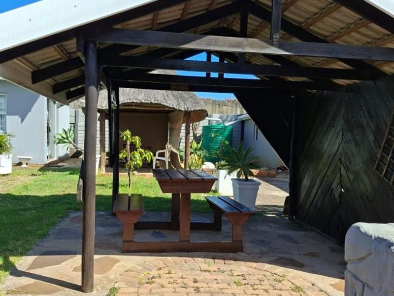 A covered outdoor patio area featuring a timber-framed roof structure and paved flooring, set within a private garden space.