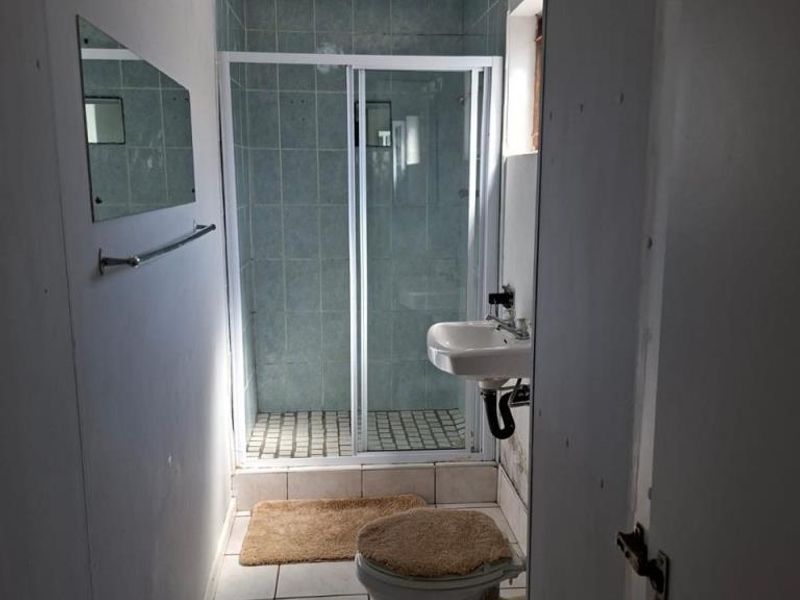 A compact bathroom featuring a shower enclosure with sliding glass doors, a wall-mounted basin, and a standard toilet with tiled flooring.