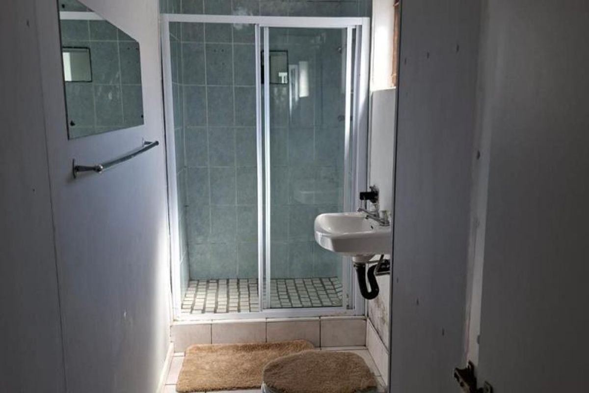 A compact bathroom featuring a shower enclosure with sliding glass doors, a wall-mounted basin, and a standard toilet with tiled flooring.