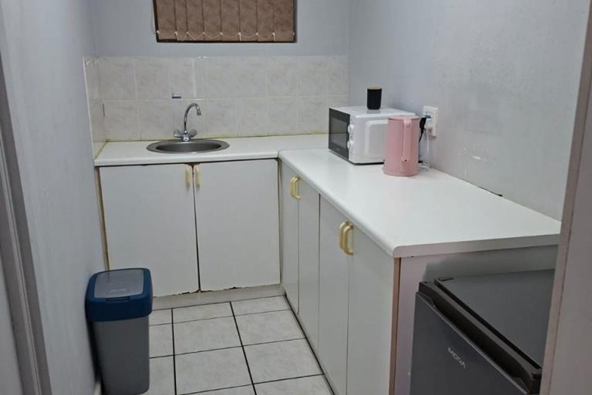 A compact kitchen featuring white cabinetry, tiled flooring, a stainless steel sink, and tiled splashback, providing a functional prep and wash-up area.