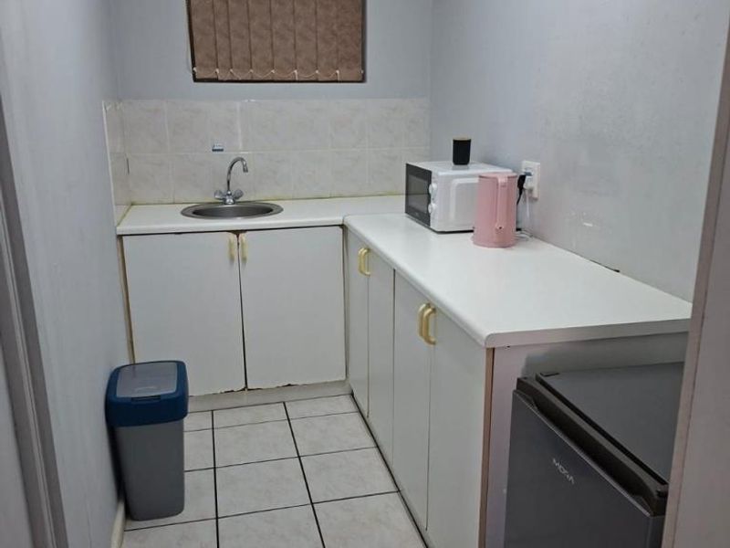 A compact kitchen featuring white cabinetry, tiled flooring, a stainless steel sink, and tiled splashback, providing a functional prep and wash-up area.