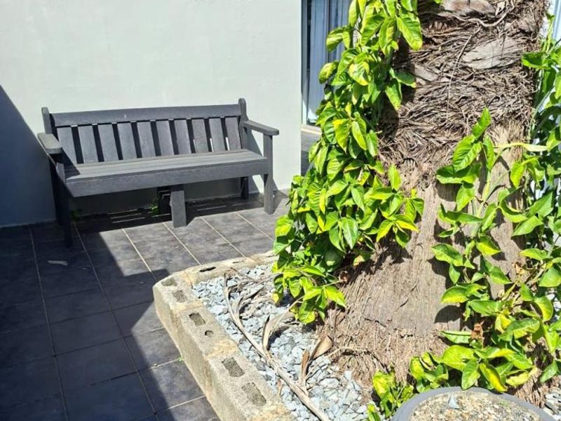 A private outdoor patio area featuring tiled flooring, a concrete planter bed, and a boundary wall, providing a quiet space for relaxation.