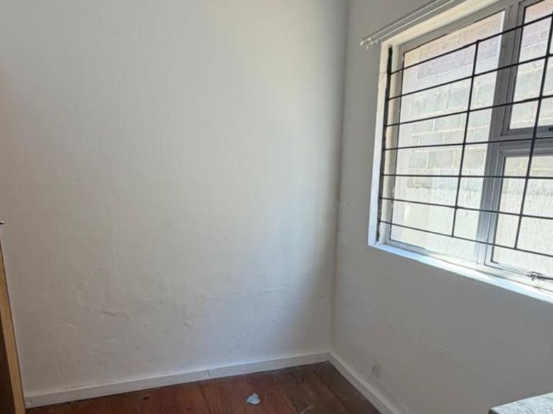 An empty bedroom featuring timber flooring, a window with security bars, and visible wall surface wear requiring maintenance.