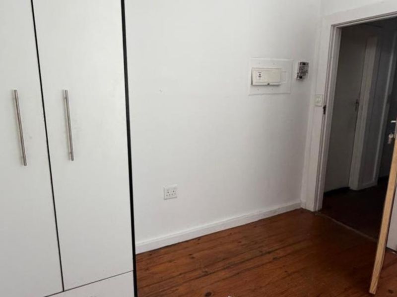 A vacant bedroom featuring timber flooring, a built-in wardrobe, and an exposed electrical distribution board, offering a blank canvas for potential updates.