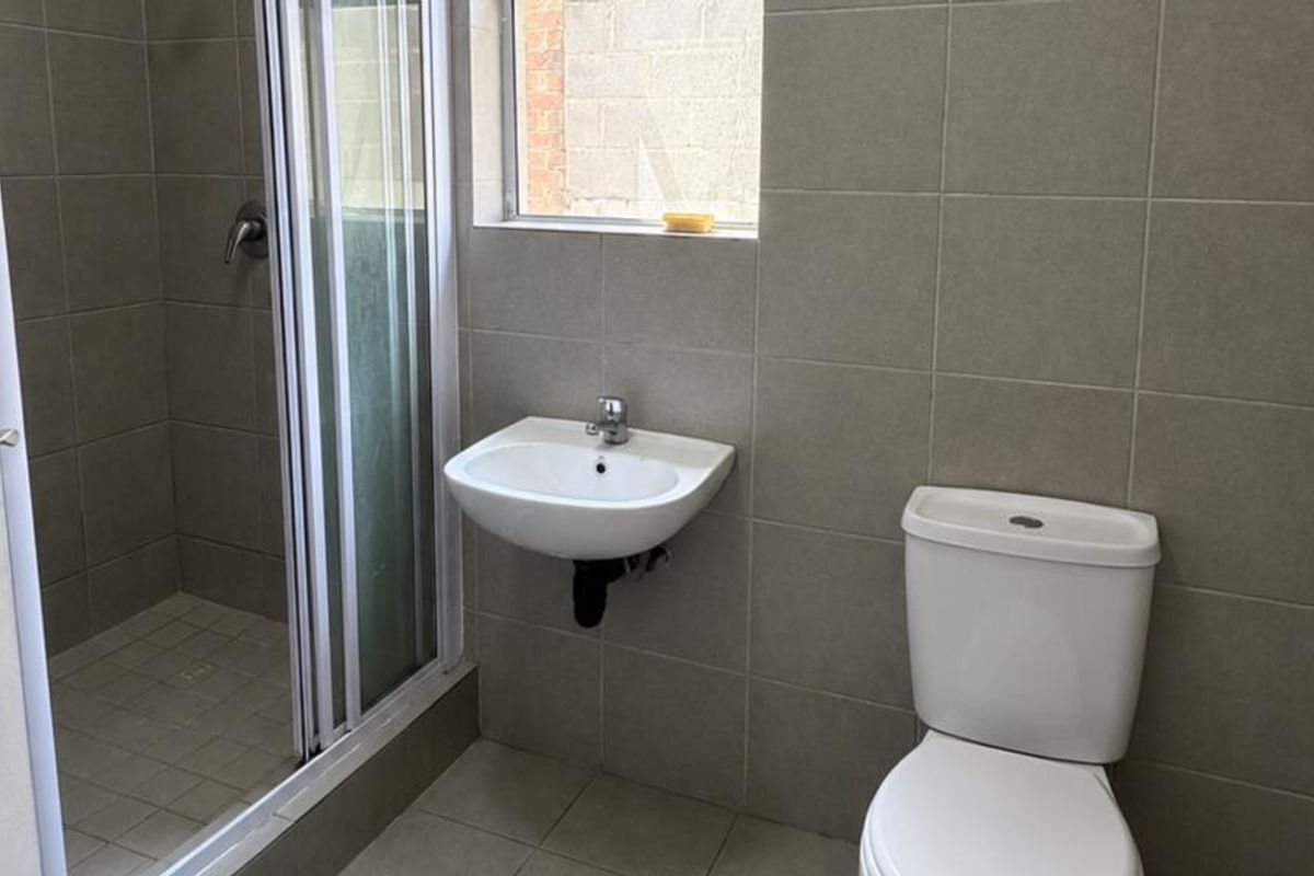 A functional bathroom featuring a shower enclosure, wall-mounted basin, and toilet with neutral wall and floor tiling.