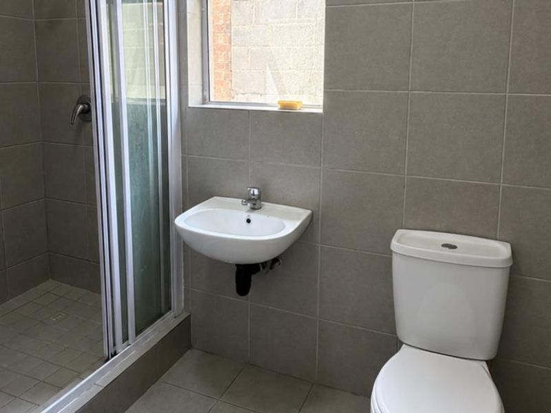 A functional bathroom featuring a shower enclosure, wall-mounted basin, and toilet with neutral wall and floor tiling.
