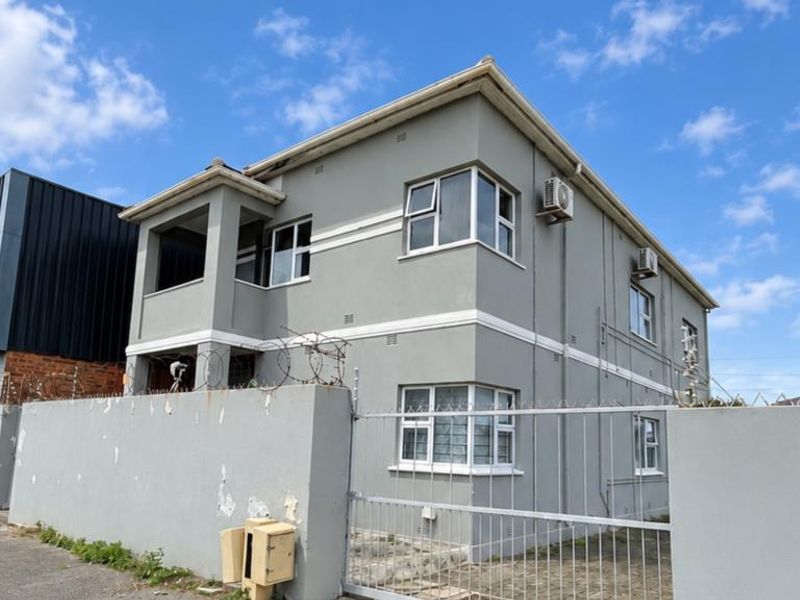 Exterior view of a two-story apartment building featuring a perimeter wall with security fencing, casement windows, and external air conditioning units.