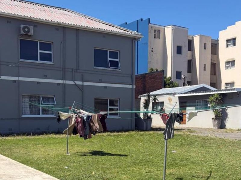 Rear view of the apartment building showing the exterior facade, paved area, and communal lawn space.