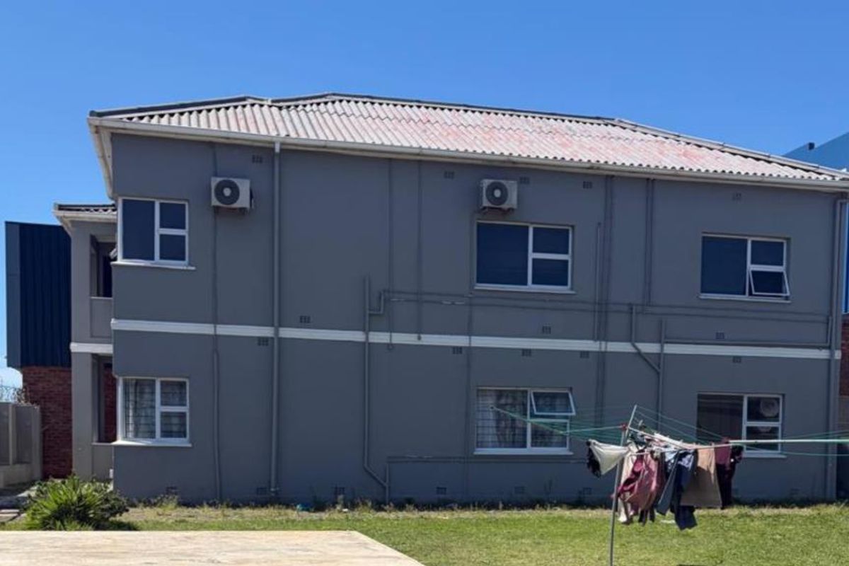 Rear elevation of a two-story apartment building featuring grey painted walls, tiled roofing, and installed air conditioning units.