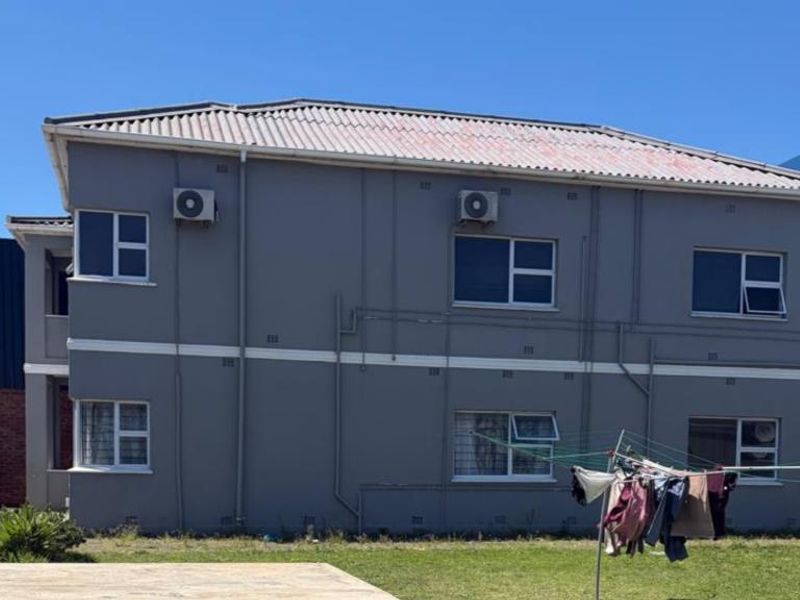 Rear elevation of a two-story apartment building featuring grey painted walls, tiled roofing, and installed air conditioning units.