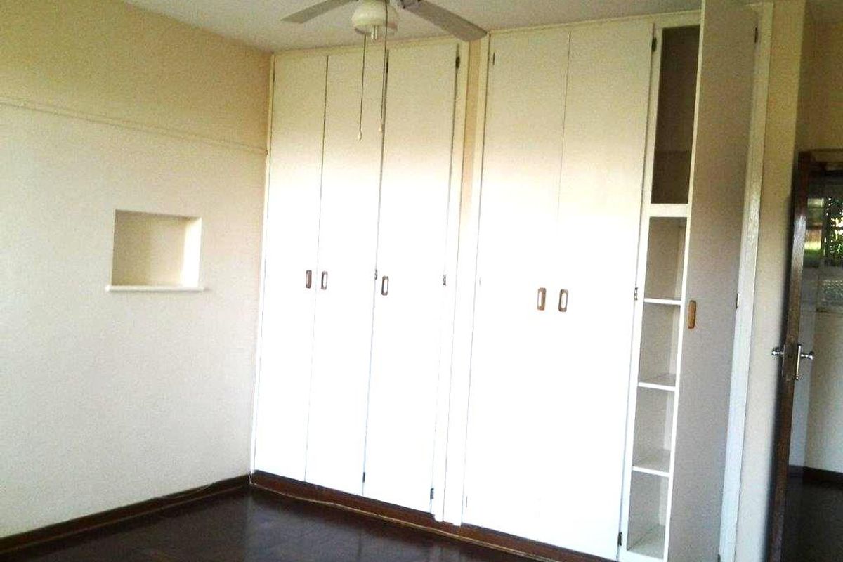 A vacant bedroom featuring original parquet flooring, a ceiling fan, and extensive built-in storage cupboards with an integrated shelving unit.