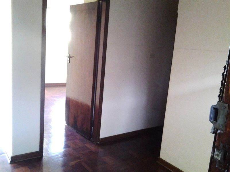 A vacant hallway featuring traditional parquet flooring and wooden door frames, showing signs of wear and requiring cosmetic updates.