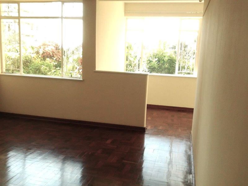 An empty living room featuring polished parquet flooring, large windows providing natural light, and a half-height partition wall separating the space.